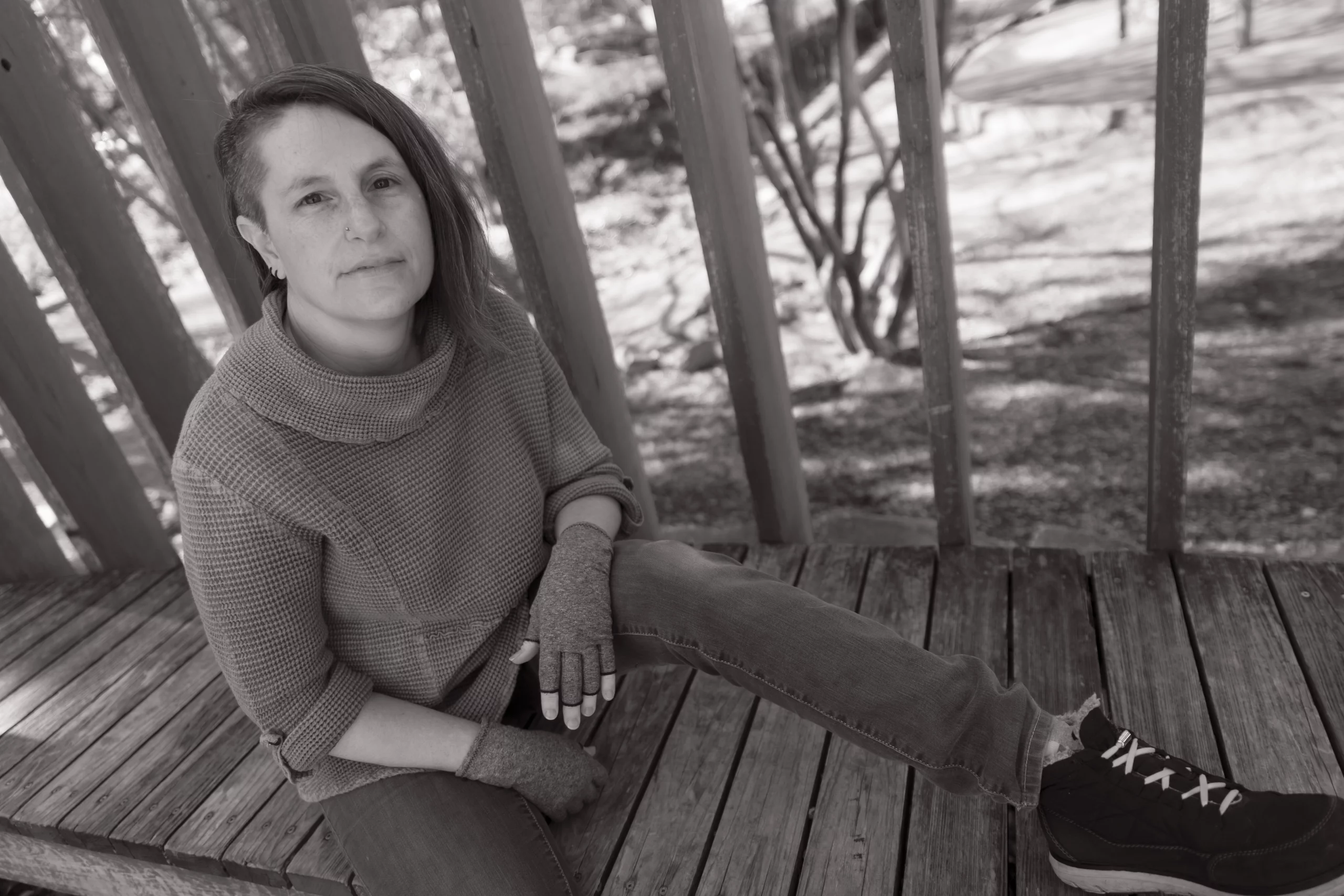 Author portrait - Caye MarshA black and white photo of an individual sitting on a wooden platform outdoors